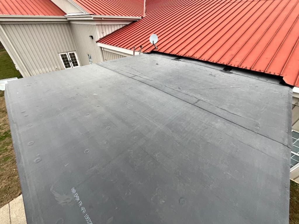 Black EPDM rubber membrane roof installation on a low-slope roof structure next to a red metal roof