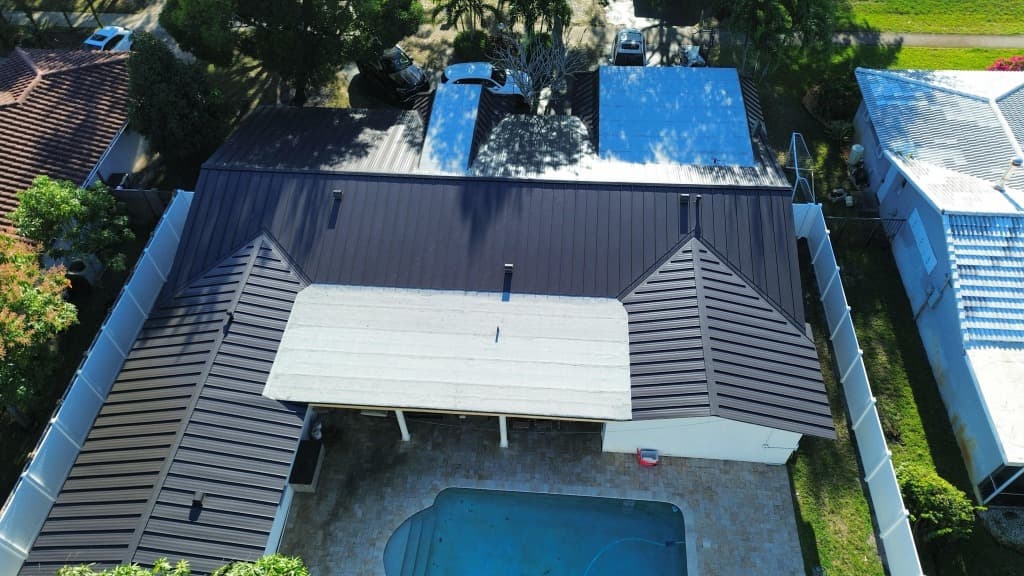 Aerial drone view of a South Florida residential home featuring a dark bronze standing seam metal roof and swimming pool
